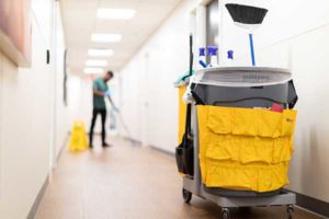 Commercial facility floor being professionally cleaned by a janitorial associate next to a caution wet floor sign