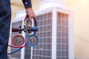 A mechanical heating and cooling equipment maintenance professional with tools stands in front of an HVAC system
